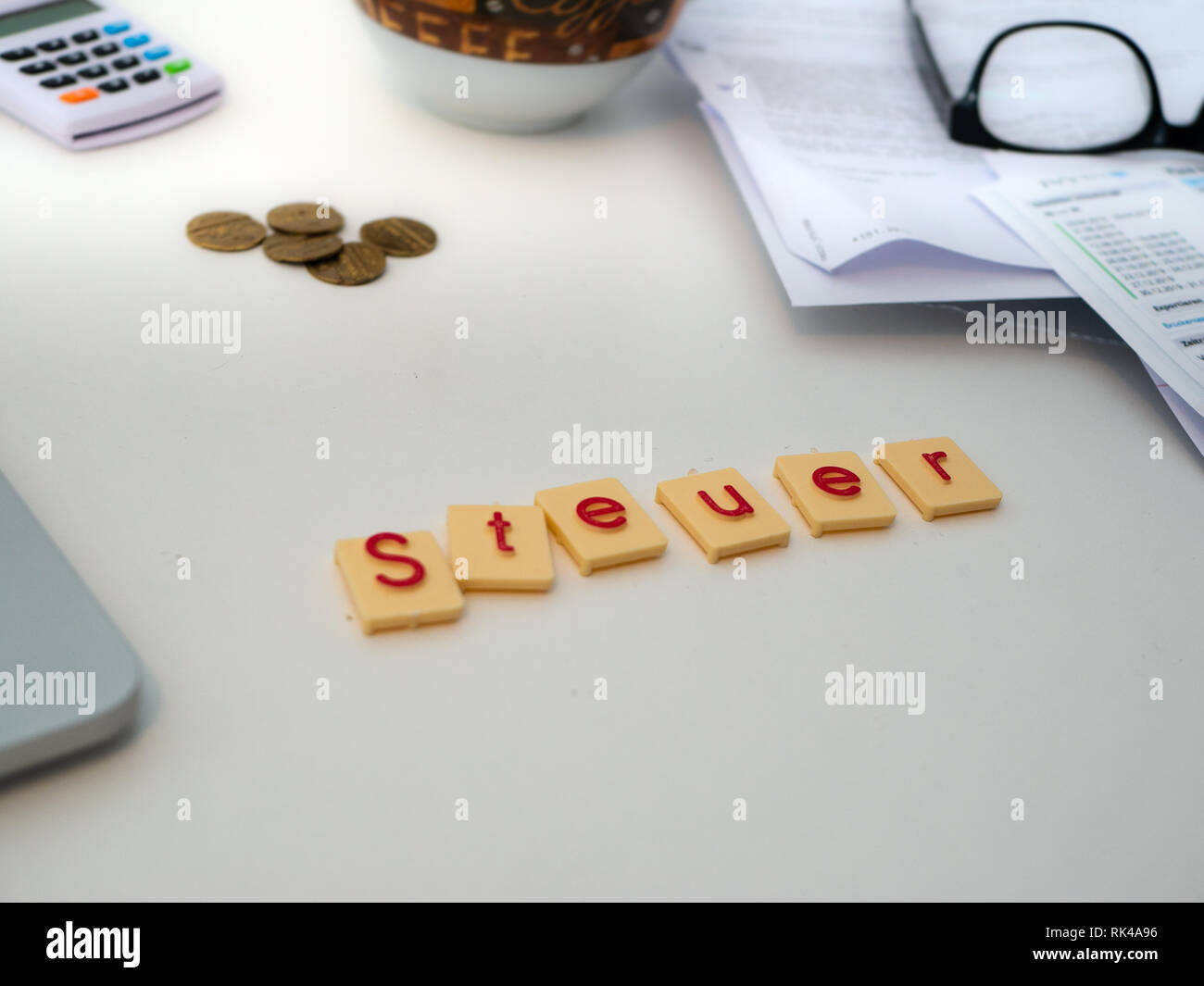 Top view of white desk with documents, glasses, notebook and letters saying "Steuer"  (Tax) Stock Photo