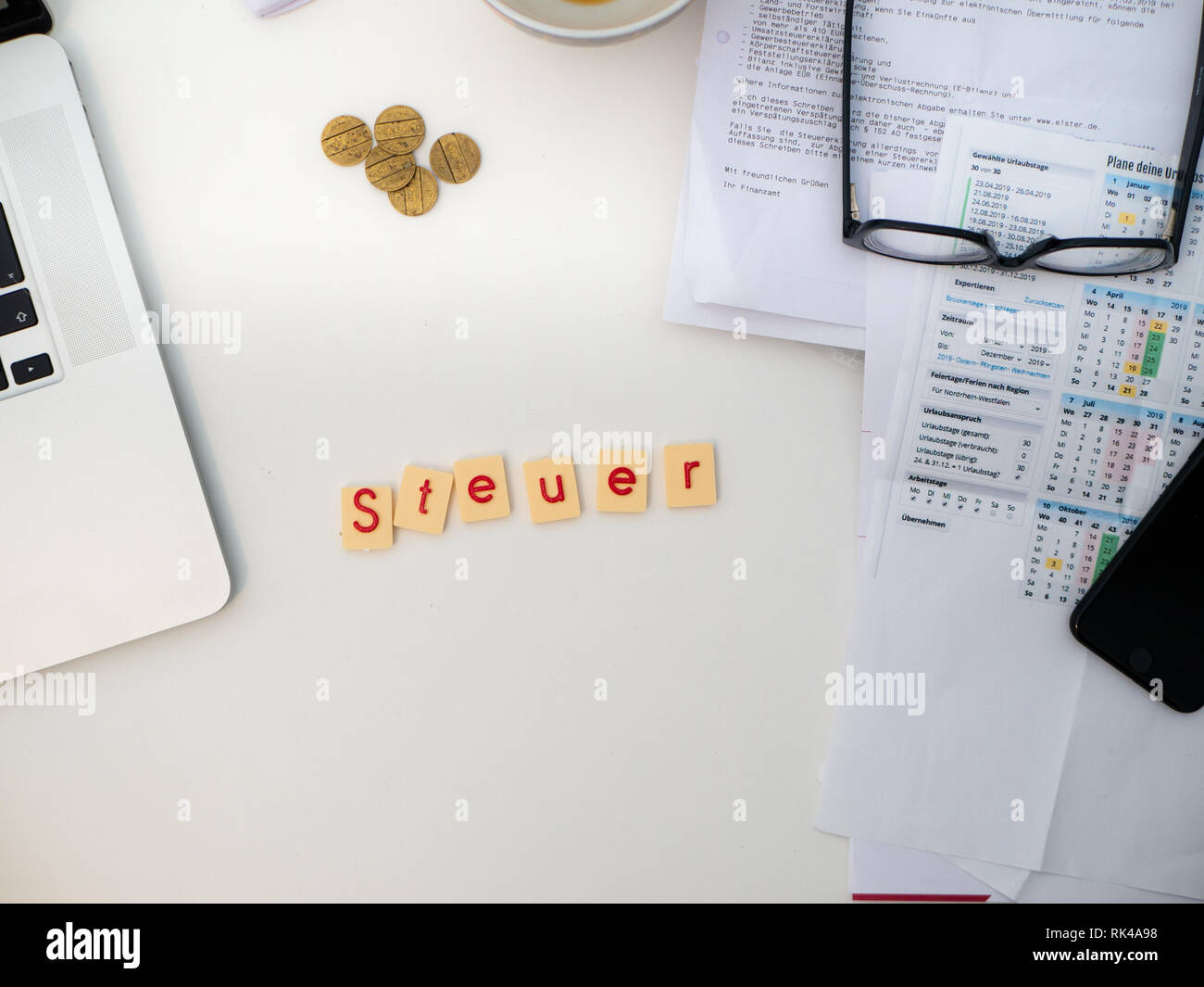 Top view of white desk with documents, glasses, notebook and letters saying 'Steuer'  (Tax) Stock Photo