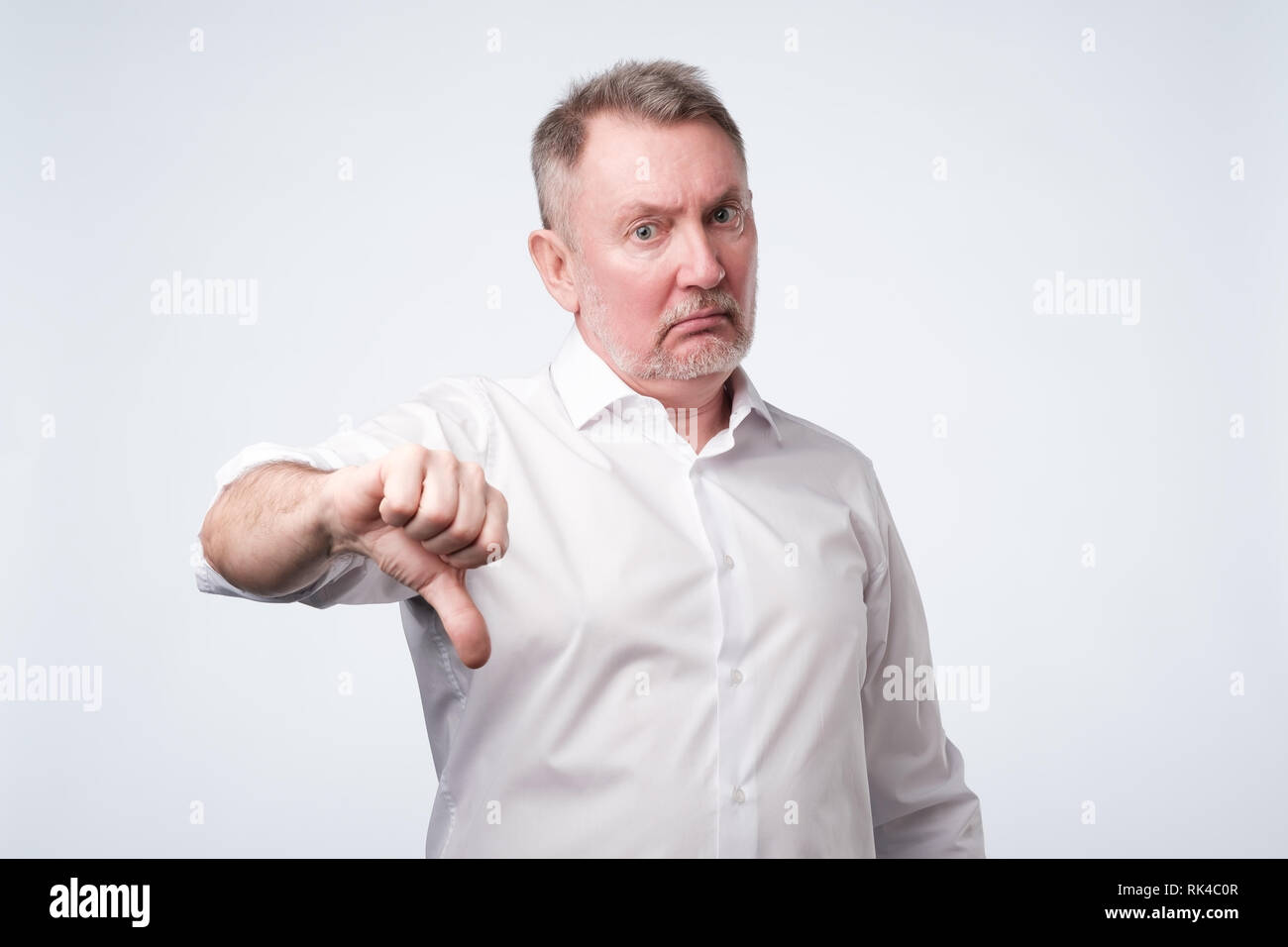 Senior man in white shirt giving thumb down Stock Photo