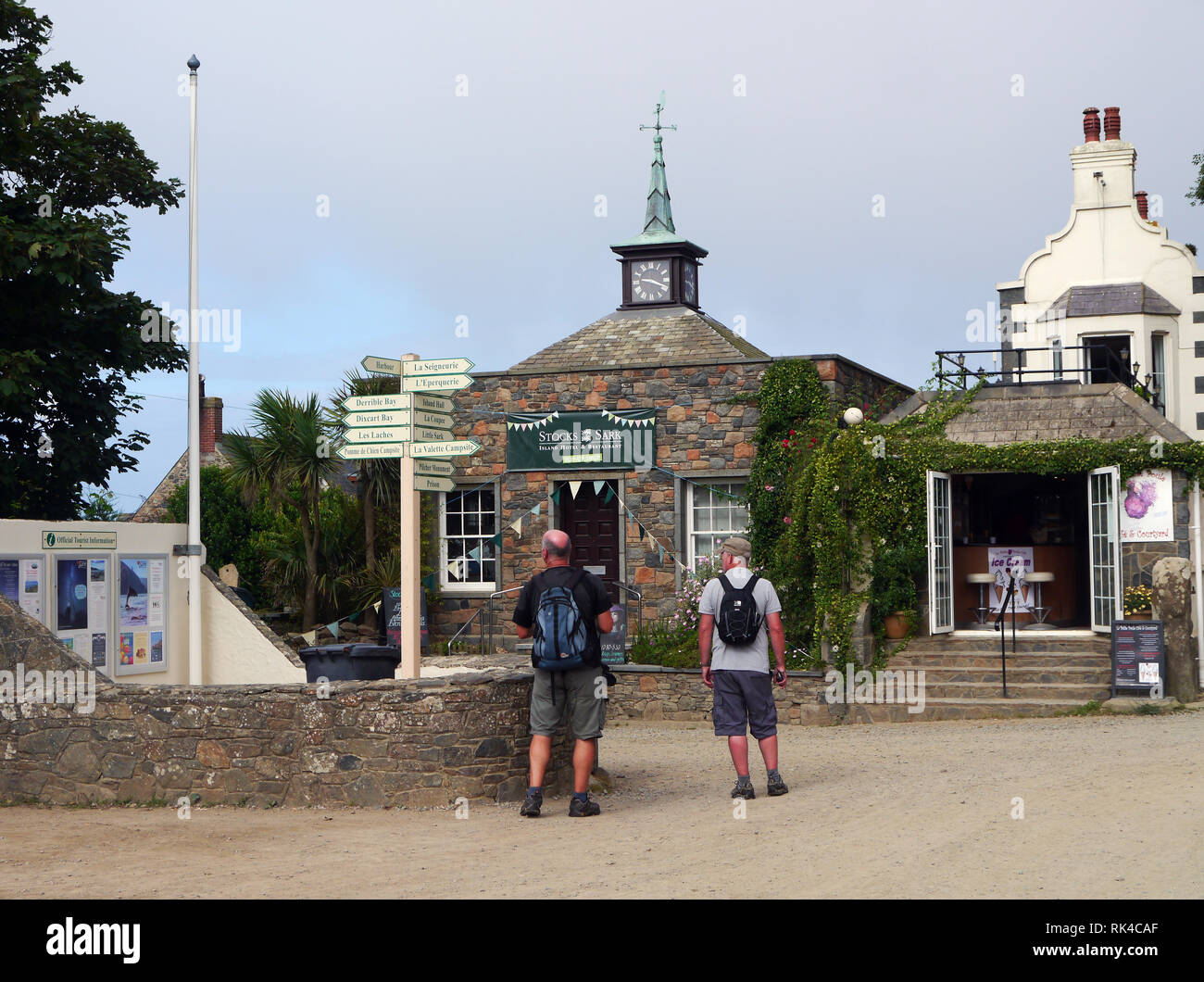 Two Men Hikers Looking at the Wooden Signpost on the Avenue in the Village at the Centre of the Island of Sark, Channel Islands, UK. Stock Photo