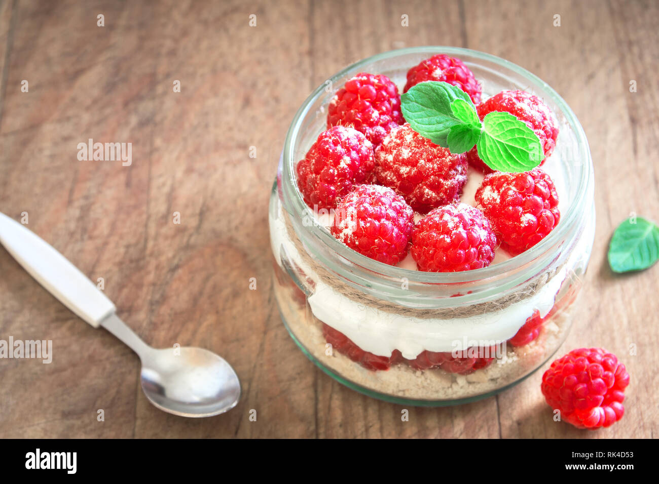 Raspberry layered dessert - cheesecake in glass jar with fresh raspberries and cream cheese. Healthy homemade summer berry dessert. Stock Photo