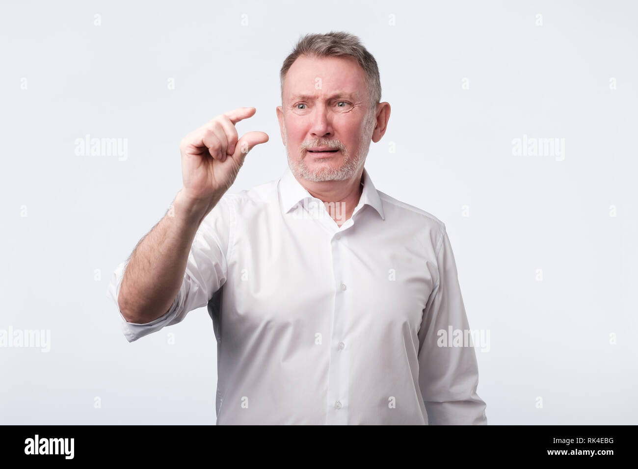 senior man shows something little with hand, demonstrates small loan. Stock Photo