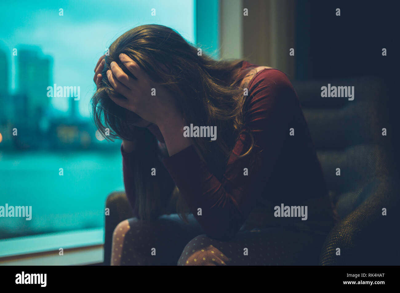 A sad woman is sitting by the window in a city Stock Photo