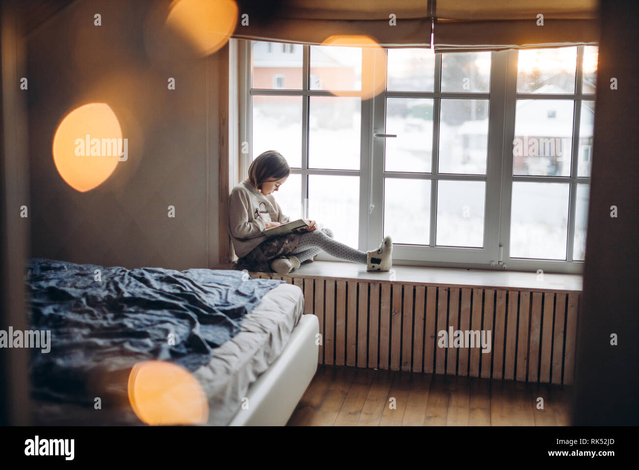 little awesome girl is doing homework on the windowsill in the bedroom. side view full length photo. loneliness. concentration Stock Photo