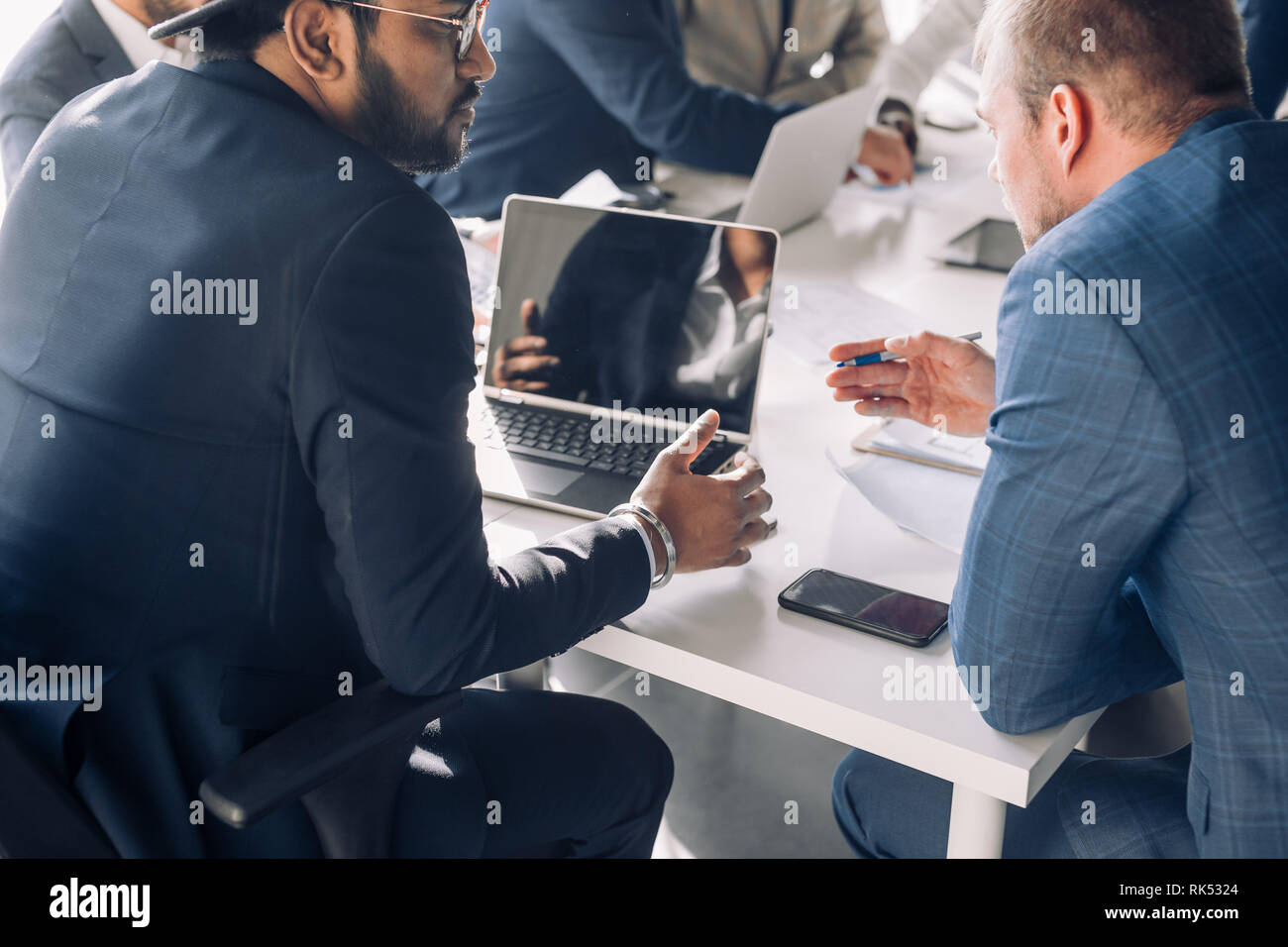 Close up top view of confident business men of different race and ages, working together, man looking on blueprint, talking, using laptop duting meeti Stock Photo