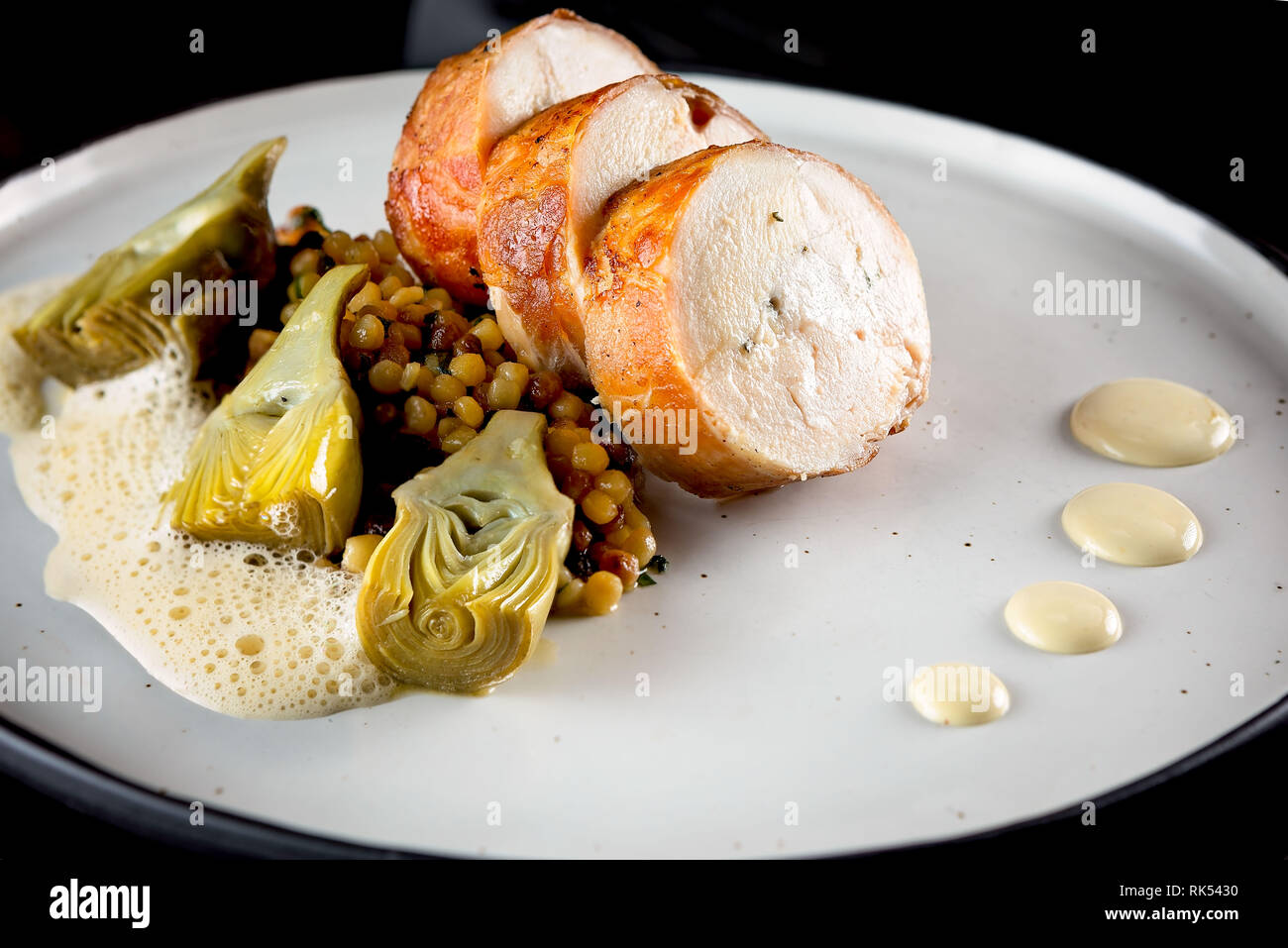 Chicken roulade with prosciutto, artichoke and emulsion on a white plate and black background Stock Photo