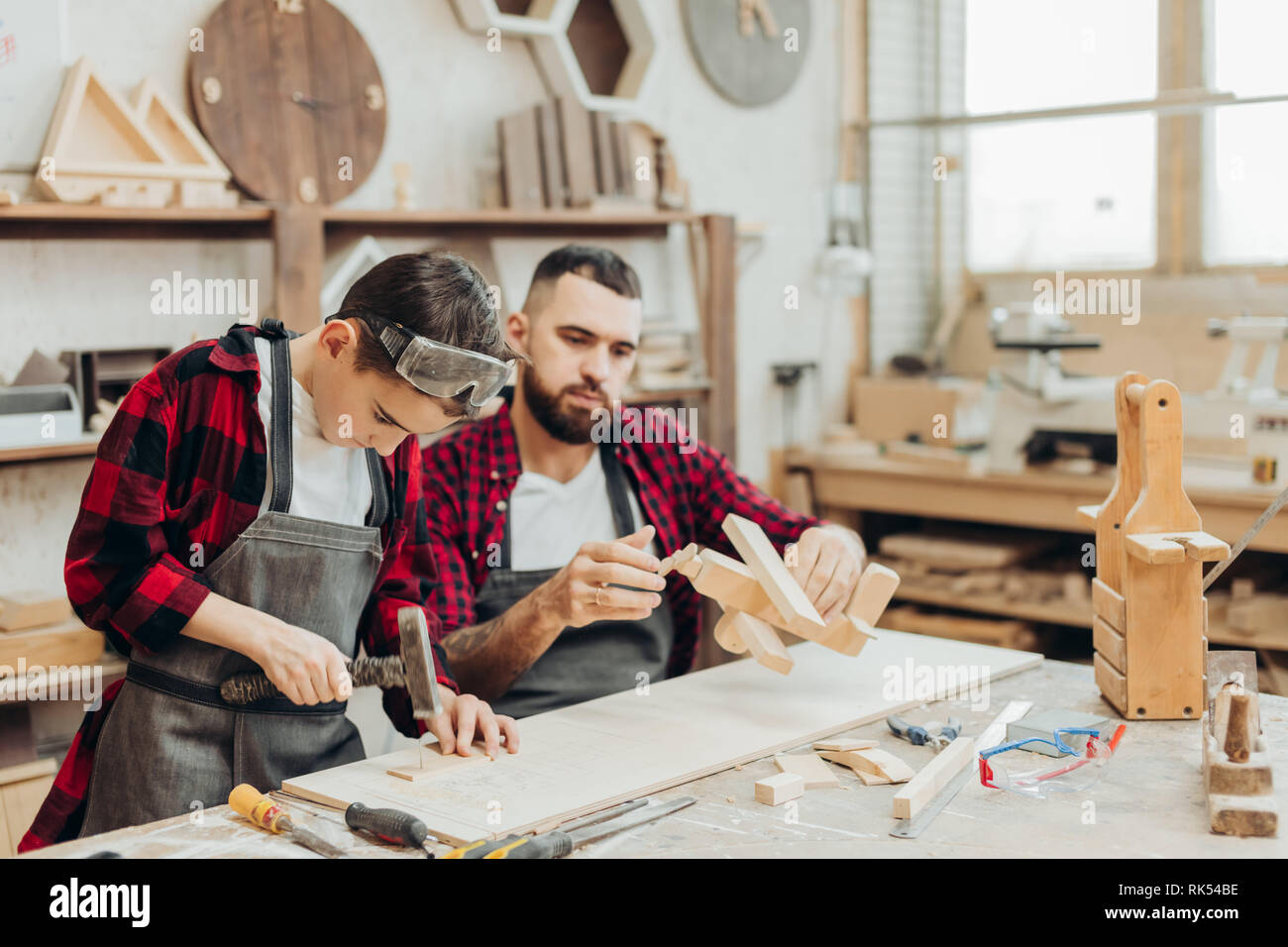 Carpenter building a wooden airplan together with his kid. A little son is participating actively in hand made process. Happy fatherhood and DIY conce Stock Photo