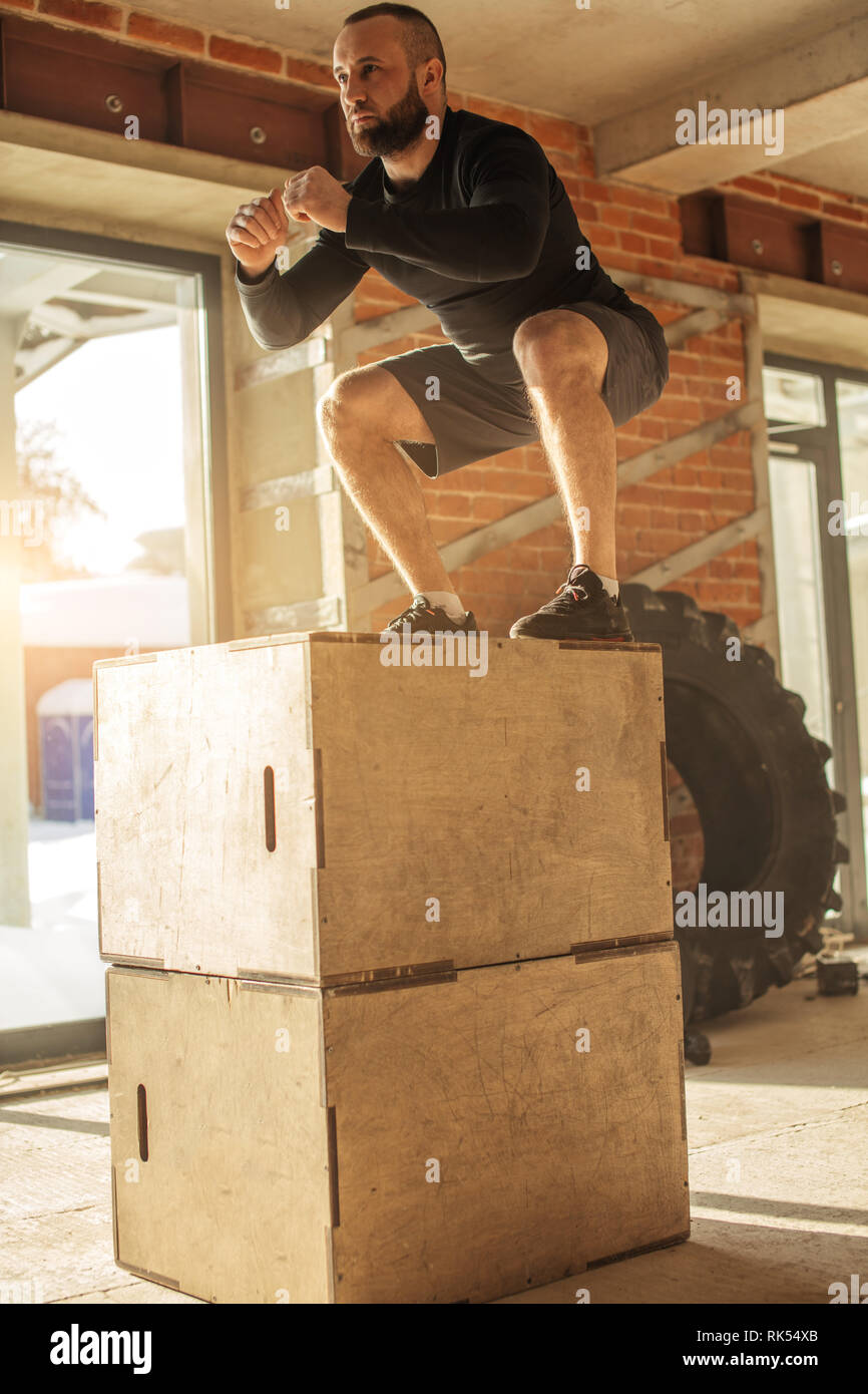 Caucasian determined sportsman performing plyometric box jumps indoor ...