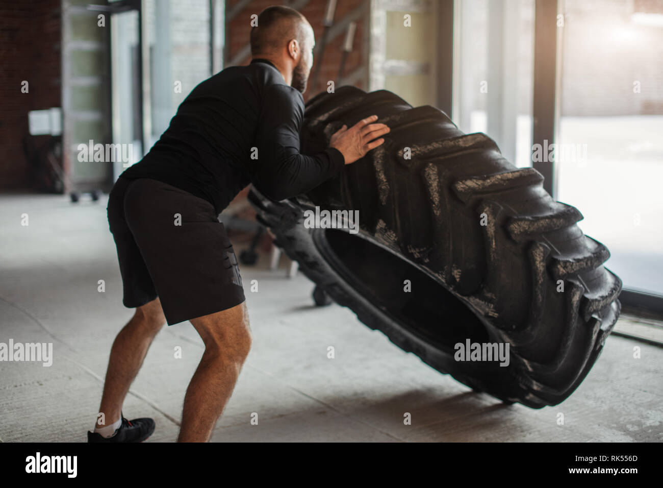 CrossFit Tire Technique. Powerful bodybuilder demonstrates rules and order of training with improvised powerlifting element in fitness club Stock Photo