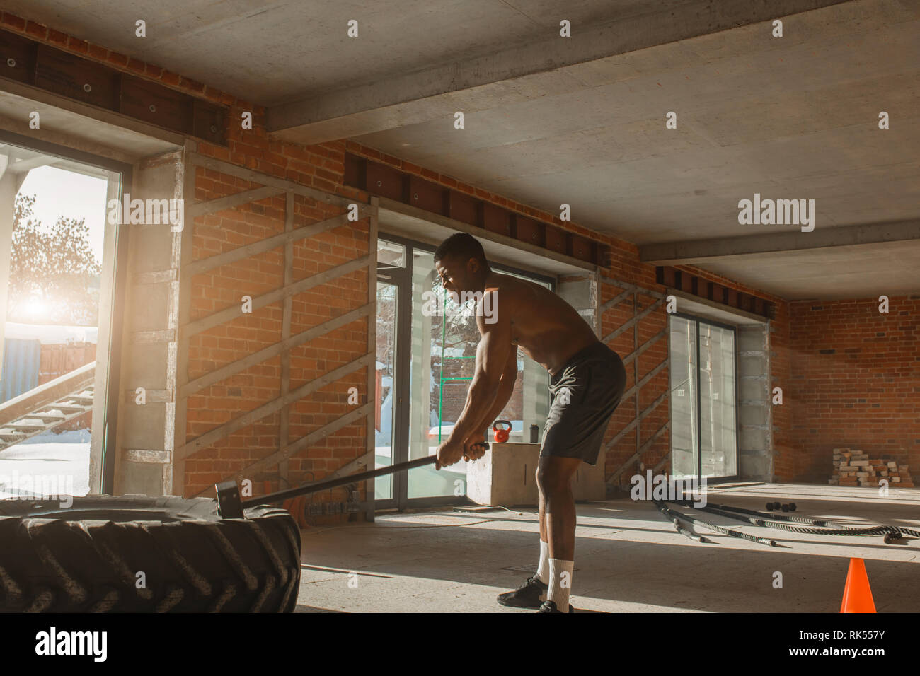 African bodybuilder exercising in hitting tire with a sledge hammer in ...