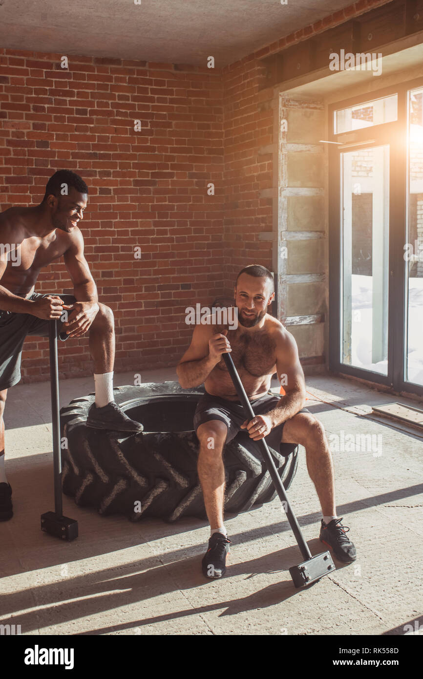 Mixed race male athletes preparing for a cross fit training with a sledgehammer and truck tire