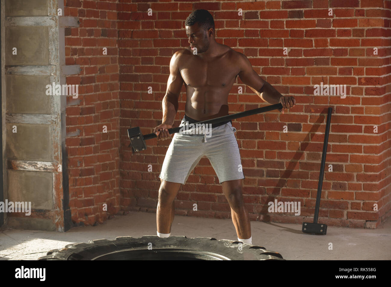 Muscular man hitting wheel tire with hammer sledge performing