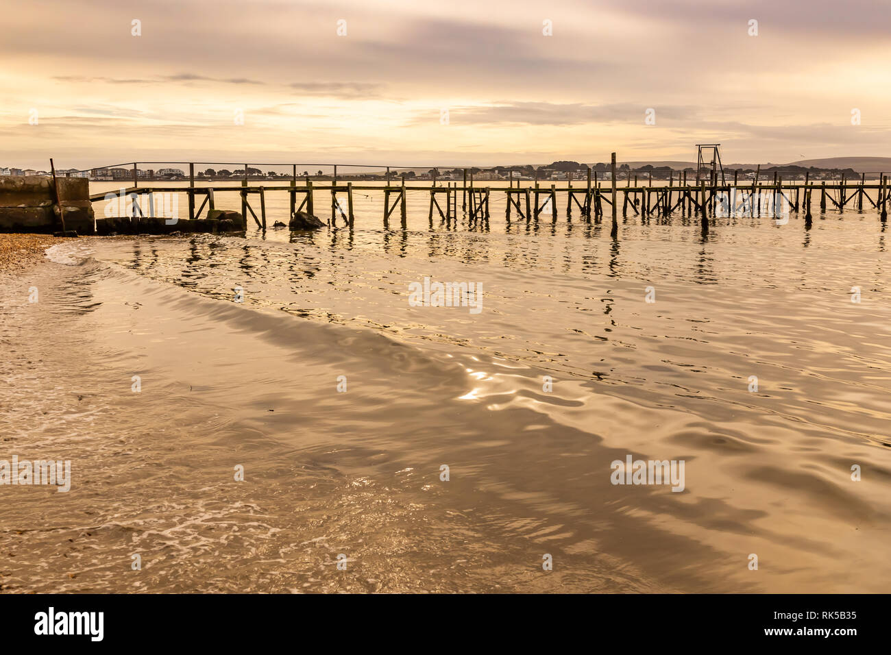Colour landscape photograph taken on Poole harbour with gently lapping waves in foreground and silhouetted pier in background, Dorset, UK. Stock Photo