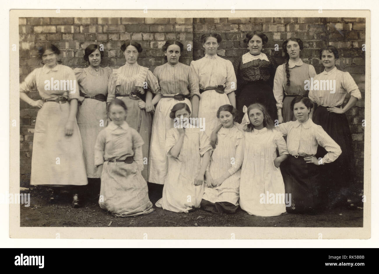 Early 1900's postcard group of cotton mill worker women and girls, tools held in belt, clogs, posing for a photograph in the mill grounds, Radcliffe, Lancashire, England, U.K. circa 1915 Stock Photo