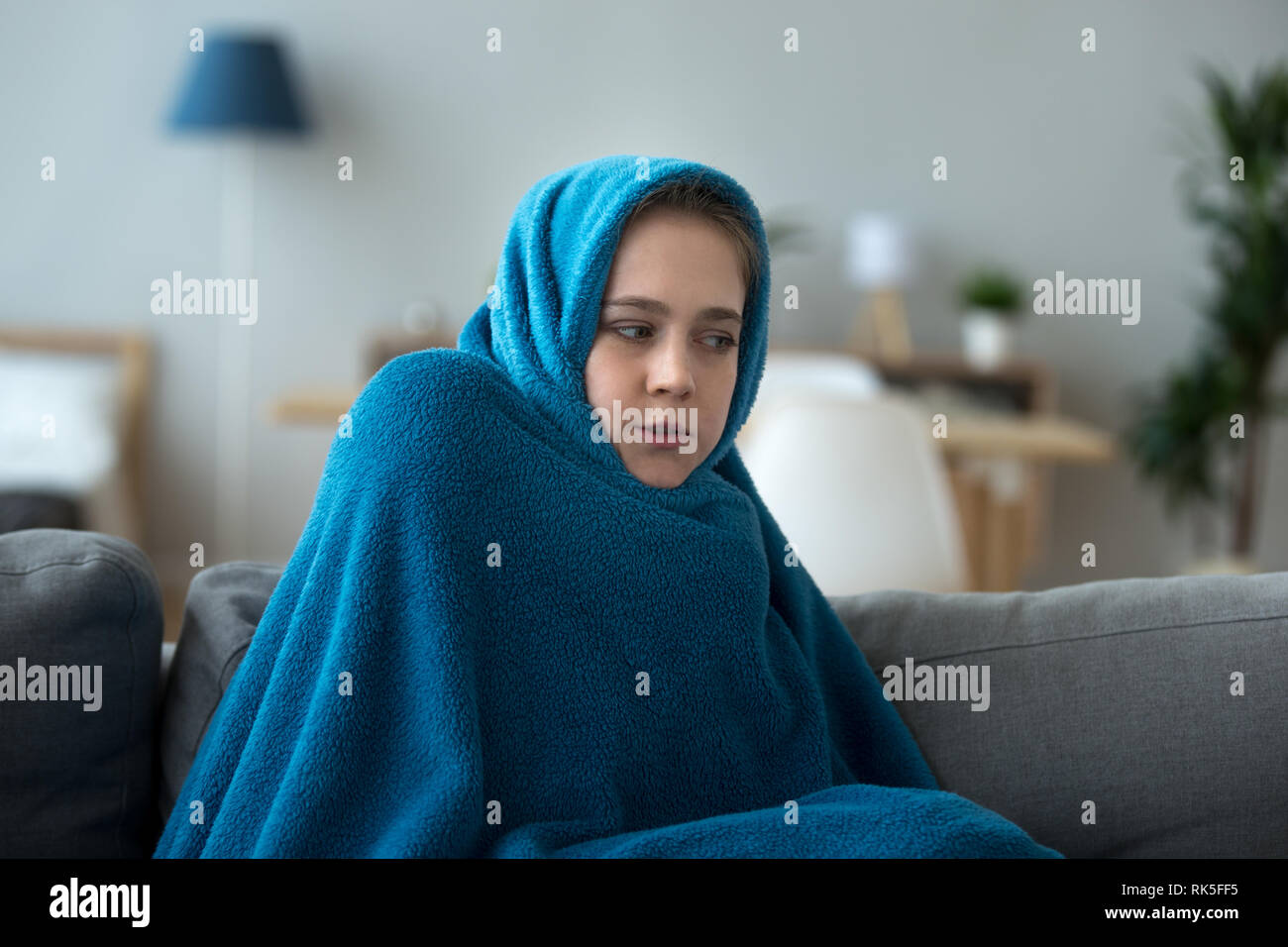 Sick young woman covered wrapped with warm blanket feeling fever Stock