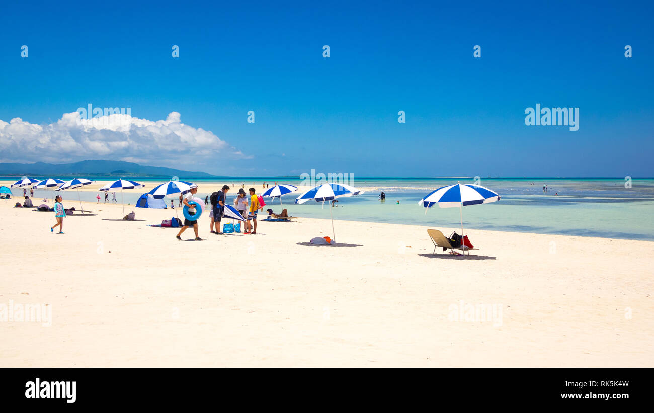 Tourists and blue and white beach umbrellas on Kondoi Beach, Taketomi Island (Taketomi-jima), Yaeyama Islands, Okinawa Prefecture, Japan. Stock Photo
