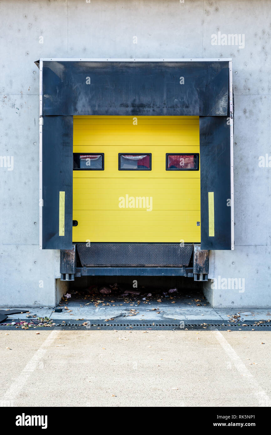 Front view of a truck loading bay with rubber seals in the concrete wall of a warehouse in the suburbs of Paris, France, with a closed yellow roller s Stock Photo