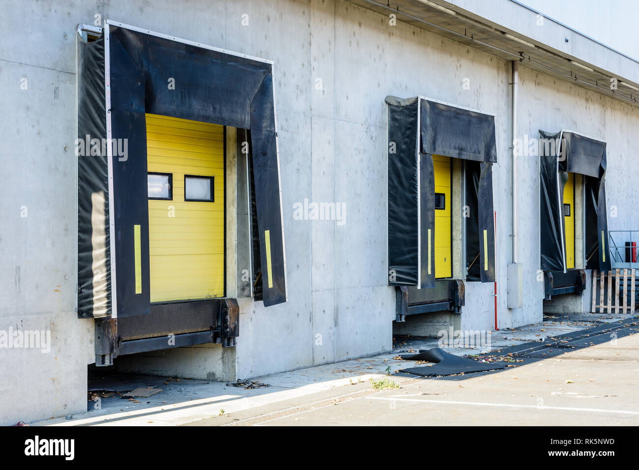 Three truck loading docks with rubber seals in the concrete wall of a warehouse with a closed yellow roller shutter door. Stock Photo