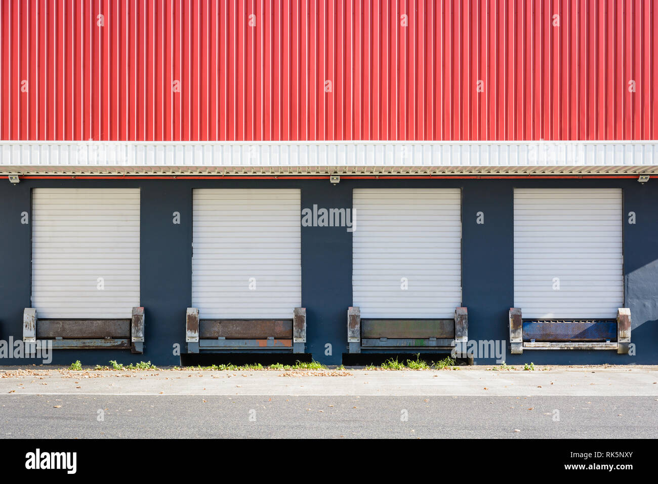 Front view of four truck loading docks at a warehouse with white roller shutter doors closed under a red corrugated iron siding. Stock Photo