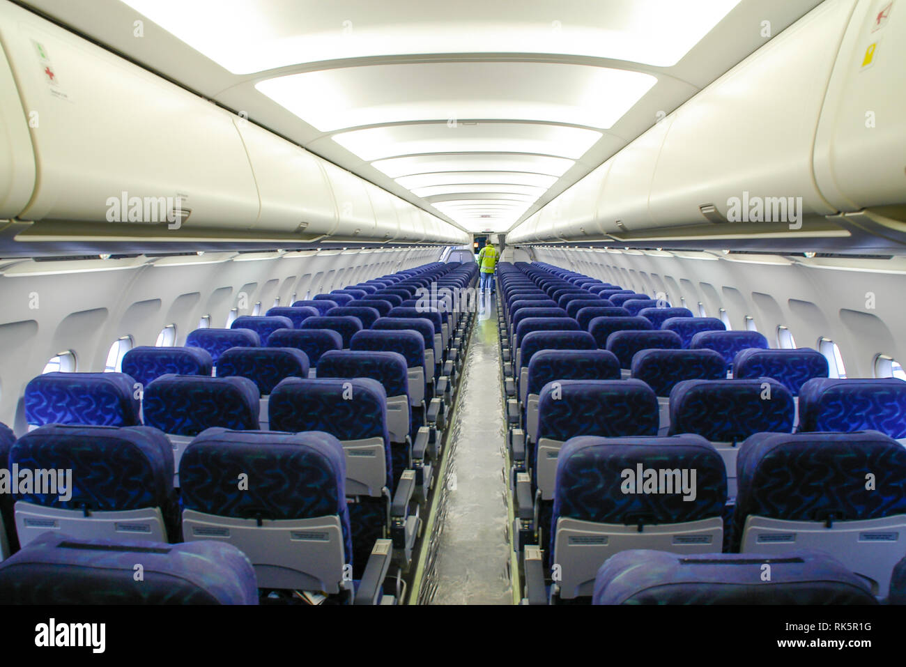 Airbus A320 cabin seats. Interior of Airbus airliner with ground support person. Seating. Overhead lockers and centre aisle layout. Empty Stock Photo