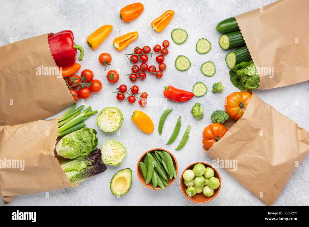 Fresh raw farm produce in paper bags, tomatoes cucumbers lettuce pepper spring onion broccoli peas on the white table, top view, selective focus Stock Photo