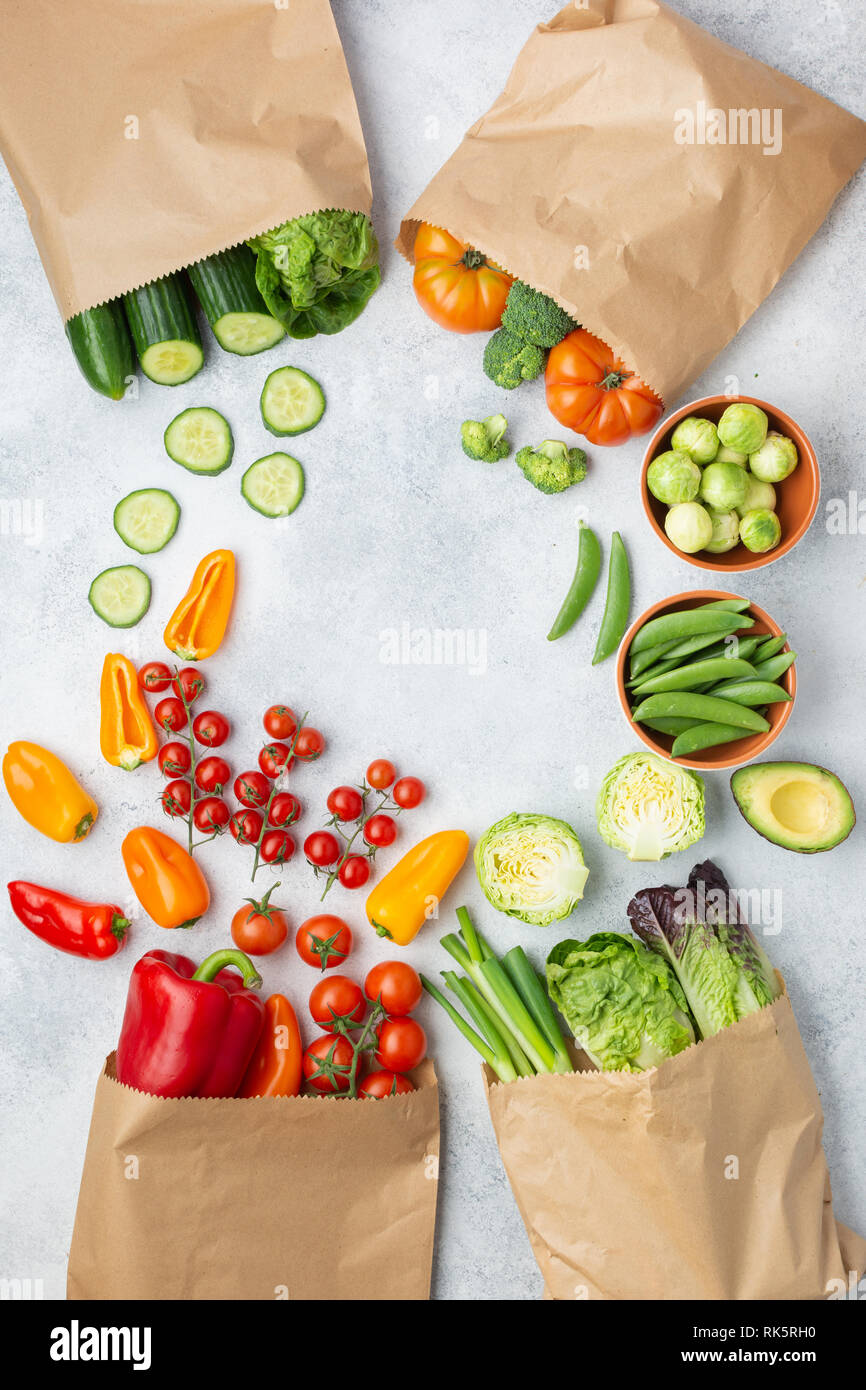 Fresh raw farm produce in paper bags, tomatoes cucumbers lettuce pepper spring onion broccoli peas on the white table, top view, copy space, selective focus Stock Photo