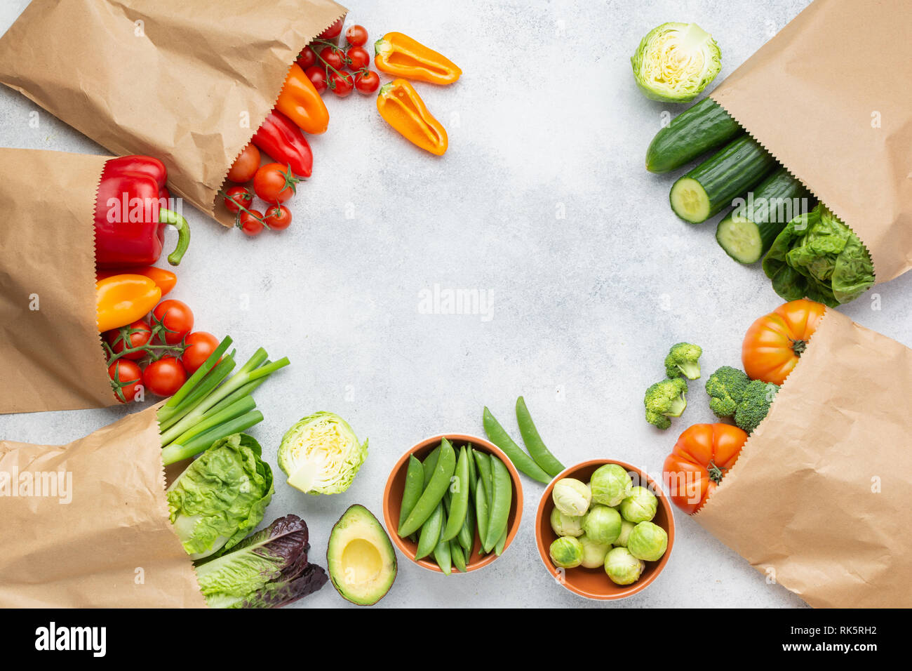 Fresh raw farm produce in paper bags, tomatoes cucumbers lettuce pepper spring onion broccoli peas on the white table, top view, copy space, selective focus Stock Photo