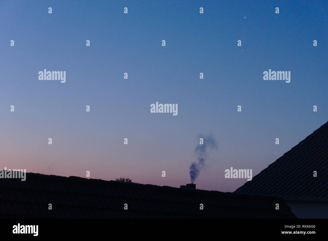 the sunset. In front the chimney of a house with smoke coming out Stock Photo