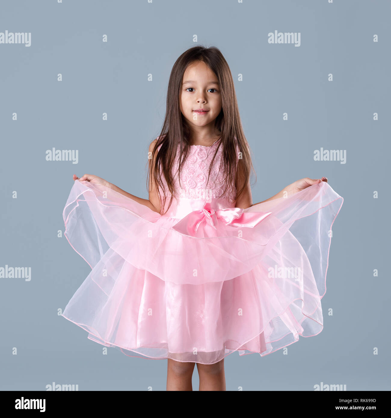 cute little child girl in pink princess dress looking at camera on gray background. Stock Photo