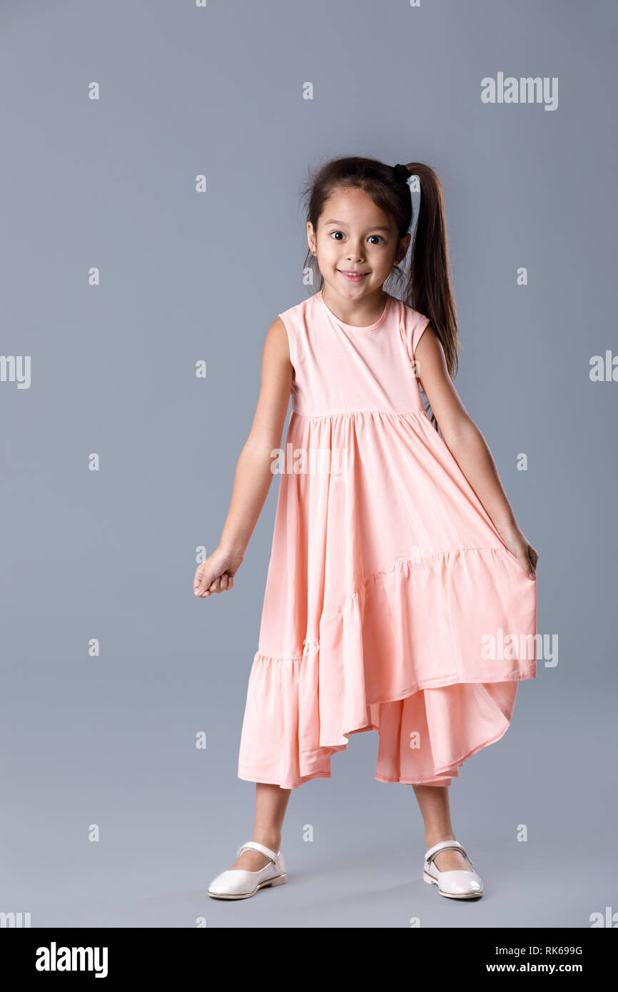 cute smiling little child girl in pink dress posing on gray background ...