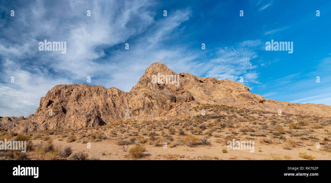 Brown desert rock formations under bright blue sky with white clouds ...