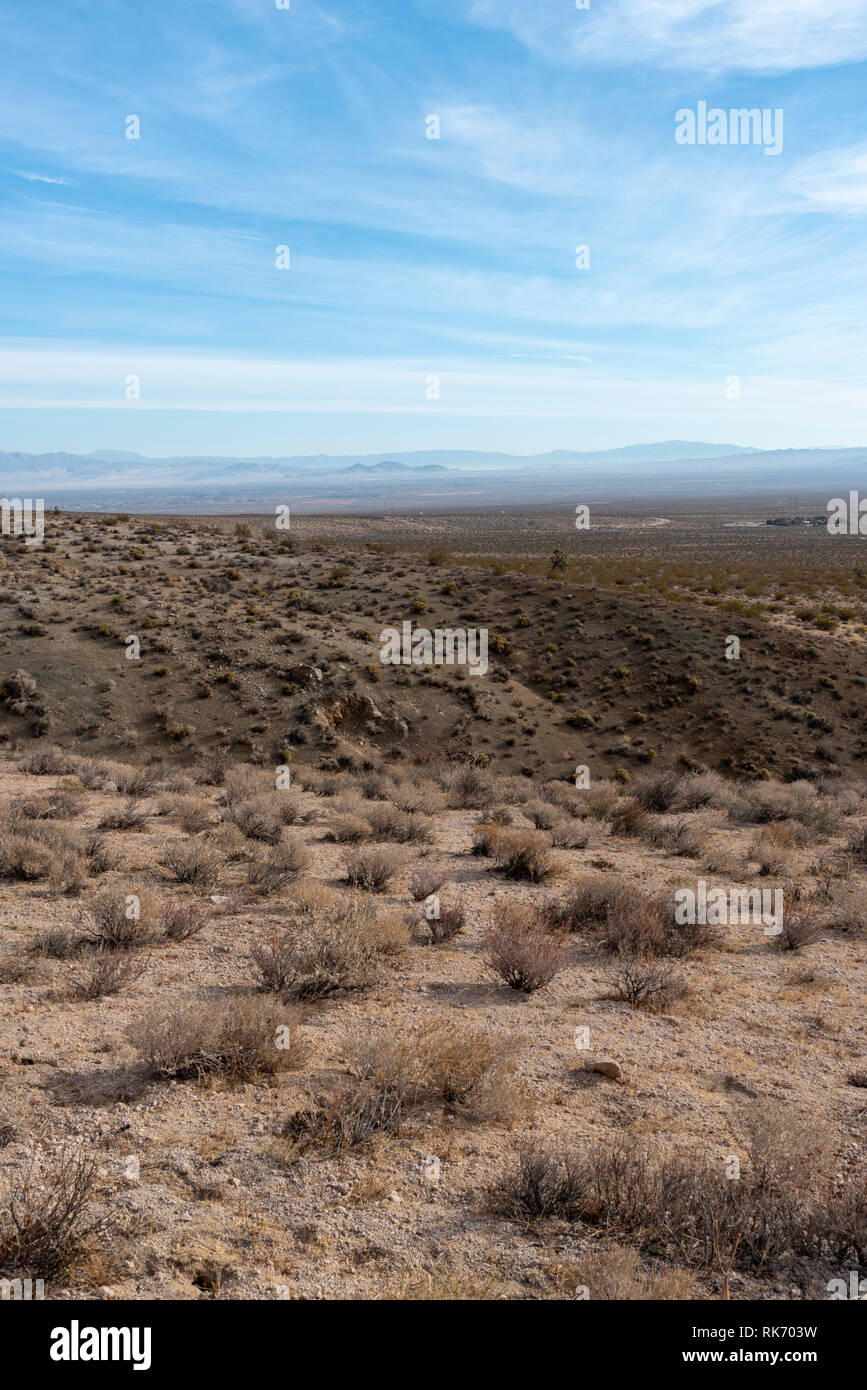 Desert valley landscape with mountains beyond under bright blue sky with white clouds. Stock Photo