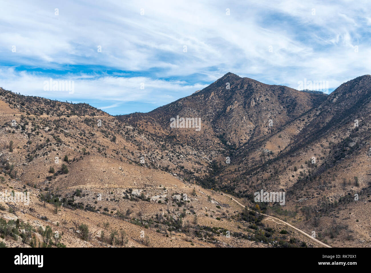 Looking across valley with mountains and trails leading to the top under bright blue sky with clouds. Sparse vegetation steep mountain sides. Stock Photo