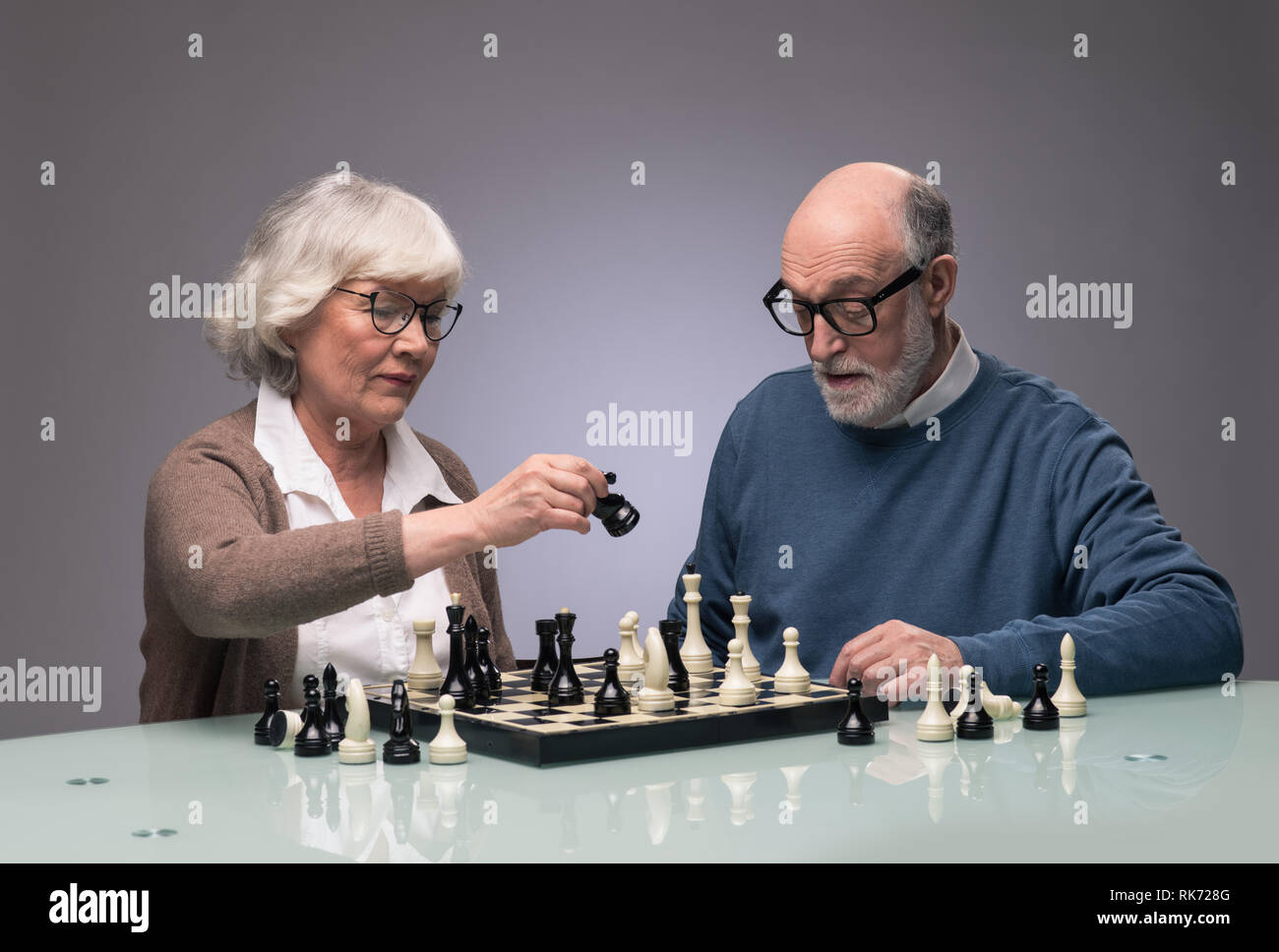 Elderly couple playing chess, studio shot on gray background Stock Photo