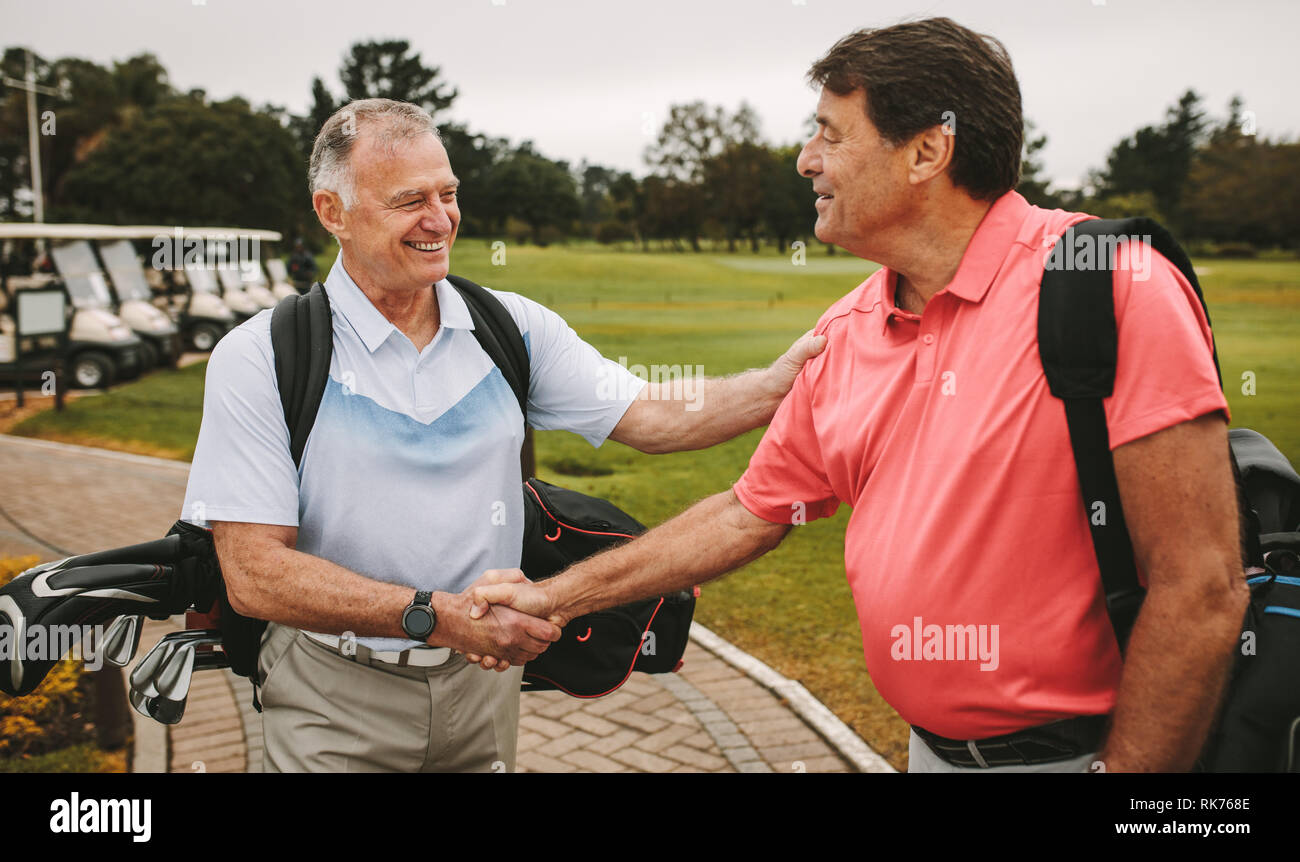 Two mature men are shaking hands and smiling when meeting on a golf course. Senior golfers at the golf course greeting each other with a handshake. Stock Photo