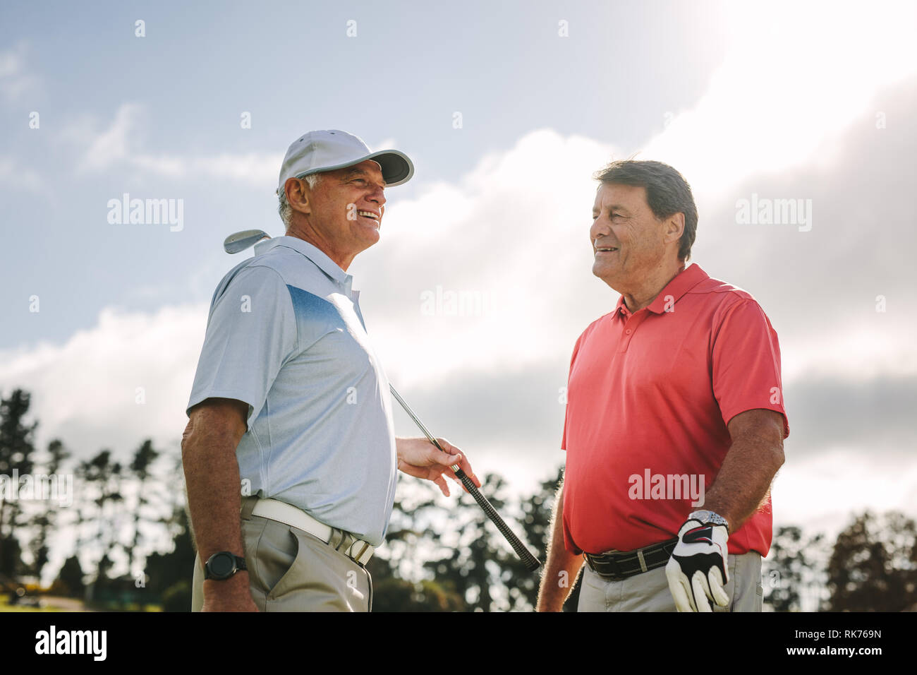 Two senior golf players with golf clubs standing together and talking between the game on a sunny day. Professional golfers having chat between the ga Stock Photo