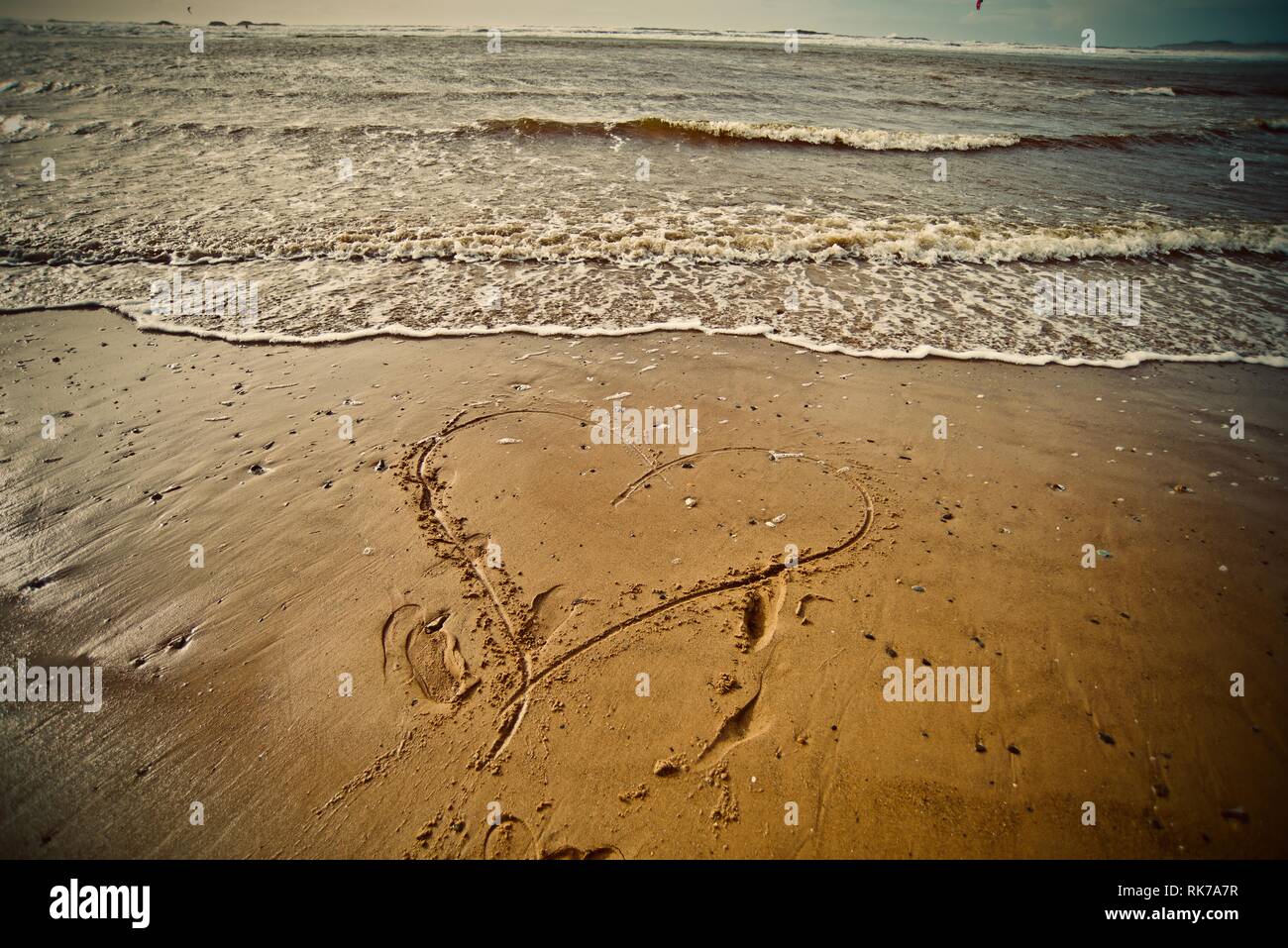 Love the beach, love the sea. A heart drawn in the sand of a beach with the tide coming in, Rhosneigr, Anglesey, North Wales, UK Stock Photo