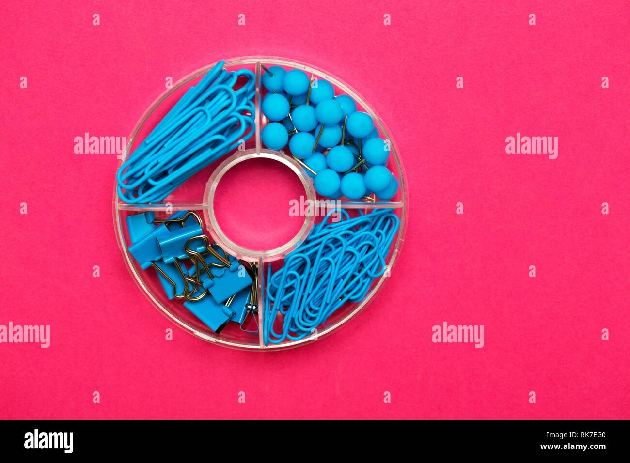stationery paper clips, binders and buttons in blue on pink background ...
