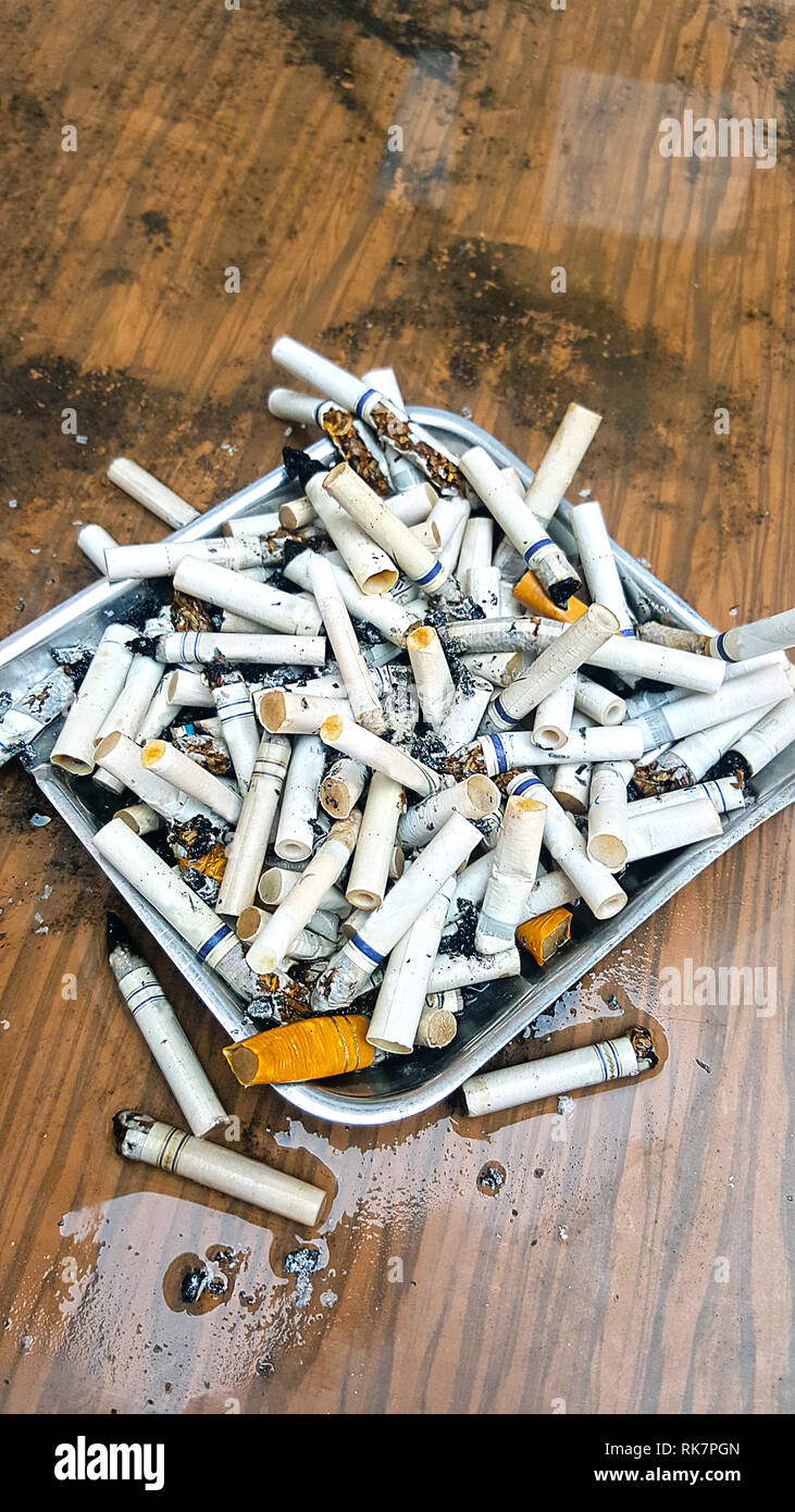 cigarette tables Top view of ashtray at outdoors on a wet dirty table full of semi-smoked  cigarettes and butts. Health and addiction concept Stock Photo
