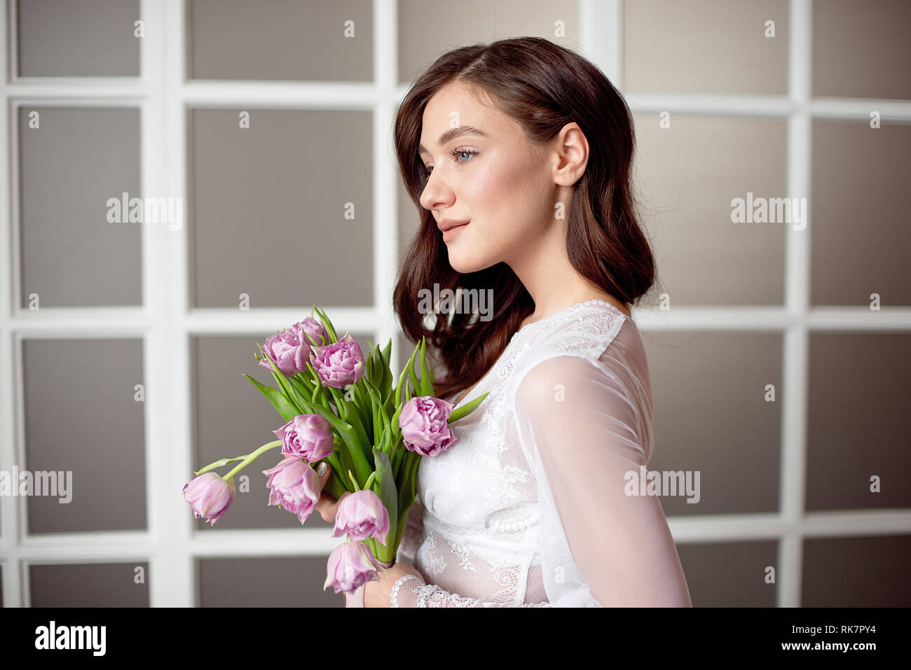Cute girl in a white lace dress holding a bouquet of flowers of tulips ...