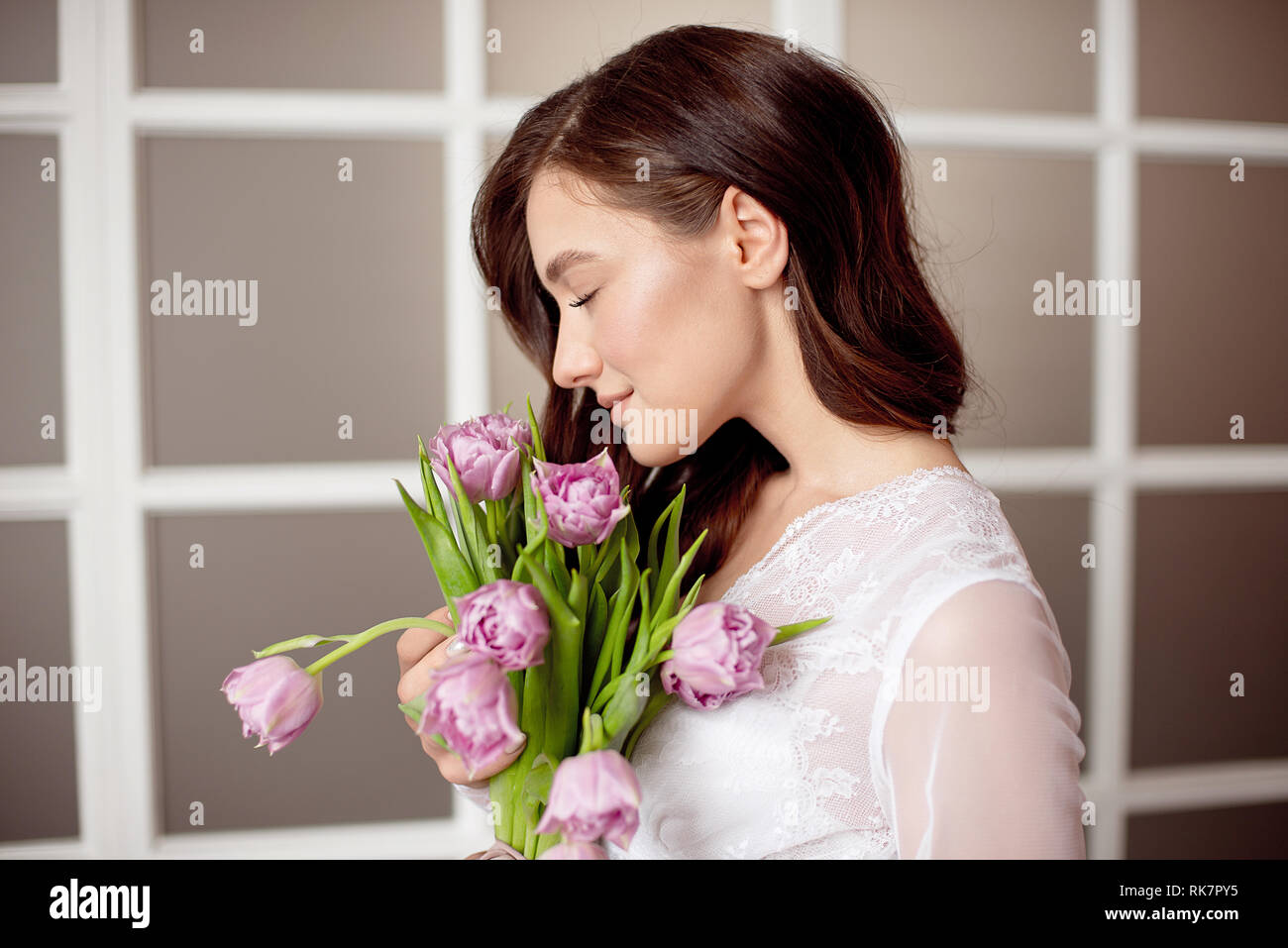 Cute girl in a white lace dress holding a bouquet of flowers of tulips ...