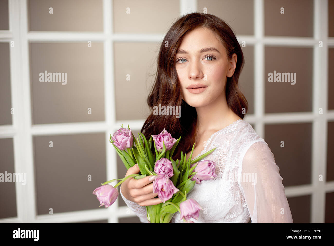 Cute girl in a white lace dress holding a bouquet of flowers of tulips ...