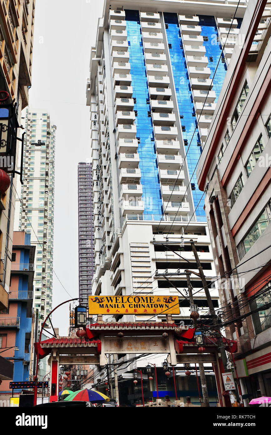 English and Chinese bilingual Welcome to Manila Chinatown poster on a concrete chinese-style arch among high-rise buildings and tangled electric wires Stock Photo