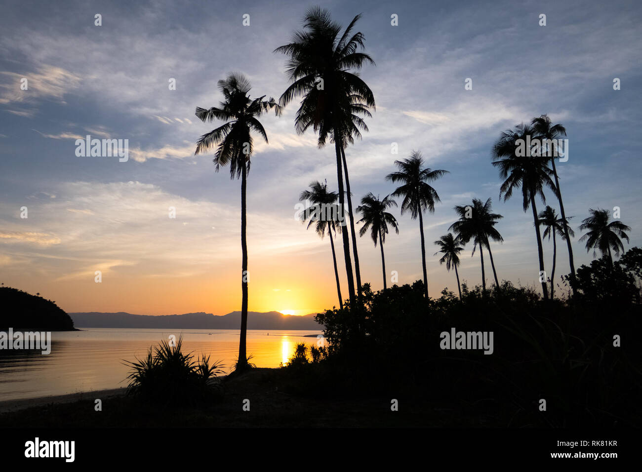 Philippines Beach Sunset with Orange Sun and Tall Palm Tree Silhouettes - Bonbon Beach, Romblon Island, Philippines. Stock Photo