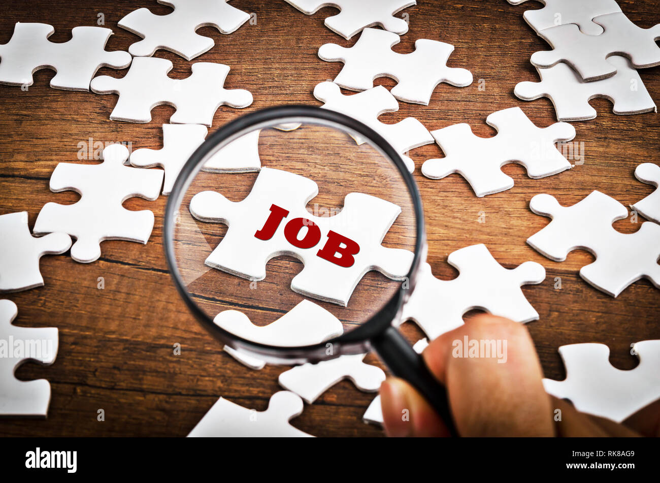 Magnifying glass searching missing puzzle piece "JOB" on wooden