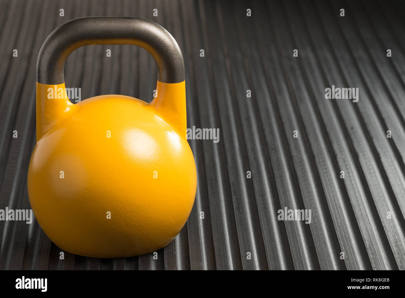 Yellow 16kg weight lifting kettlebell inside a gym. Copy space to the right of kettlebell. Stock Photo