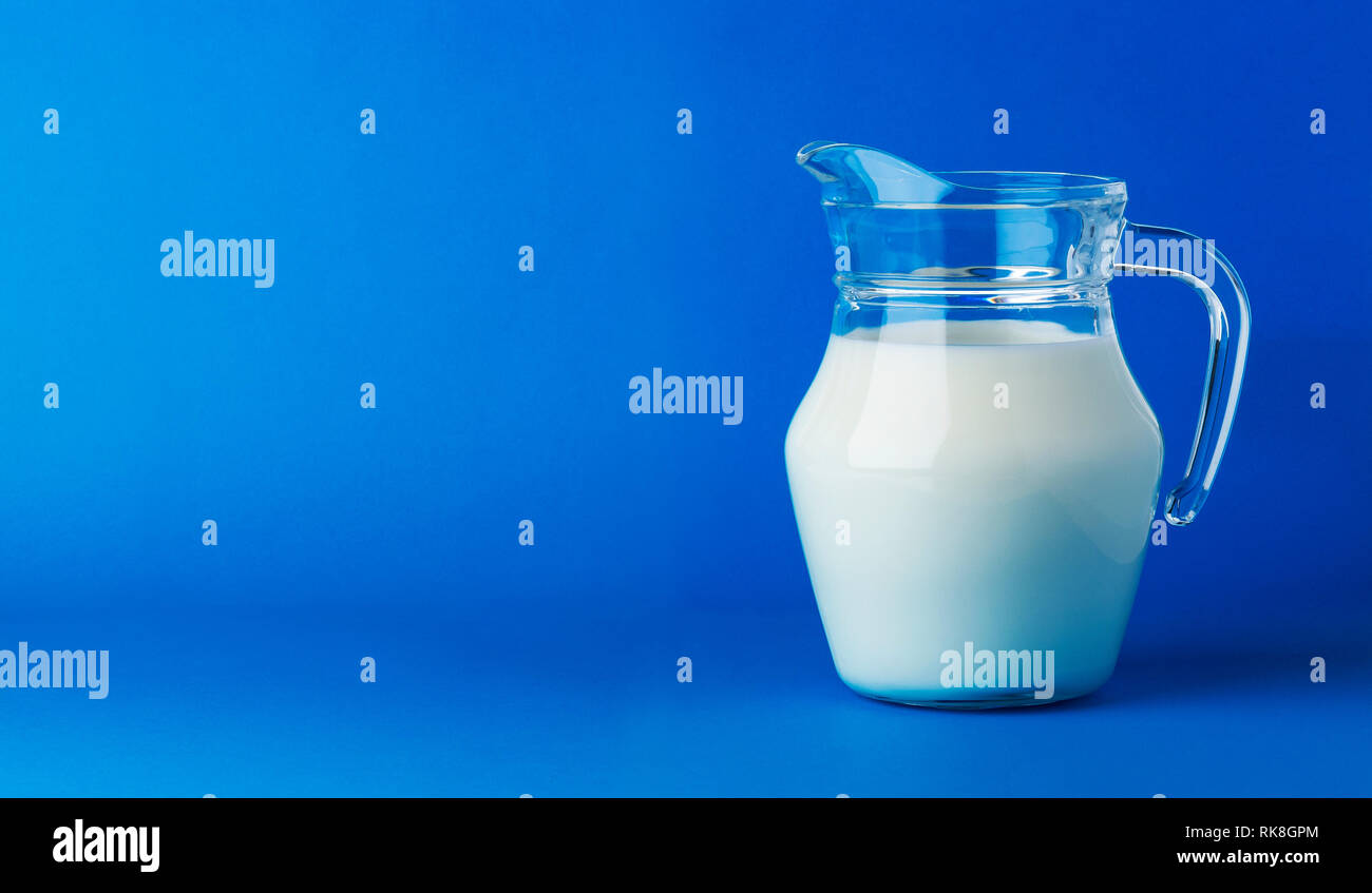 Glass jug of milk isolated on blue background with copy space Stock