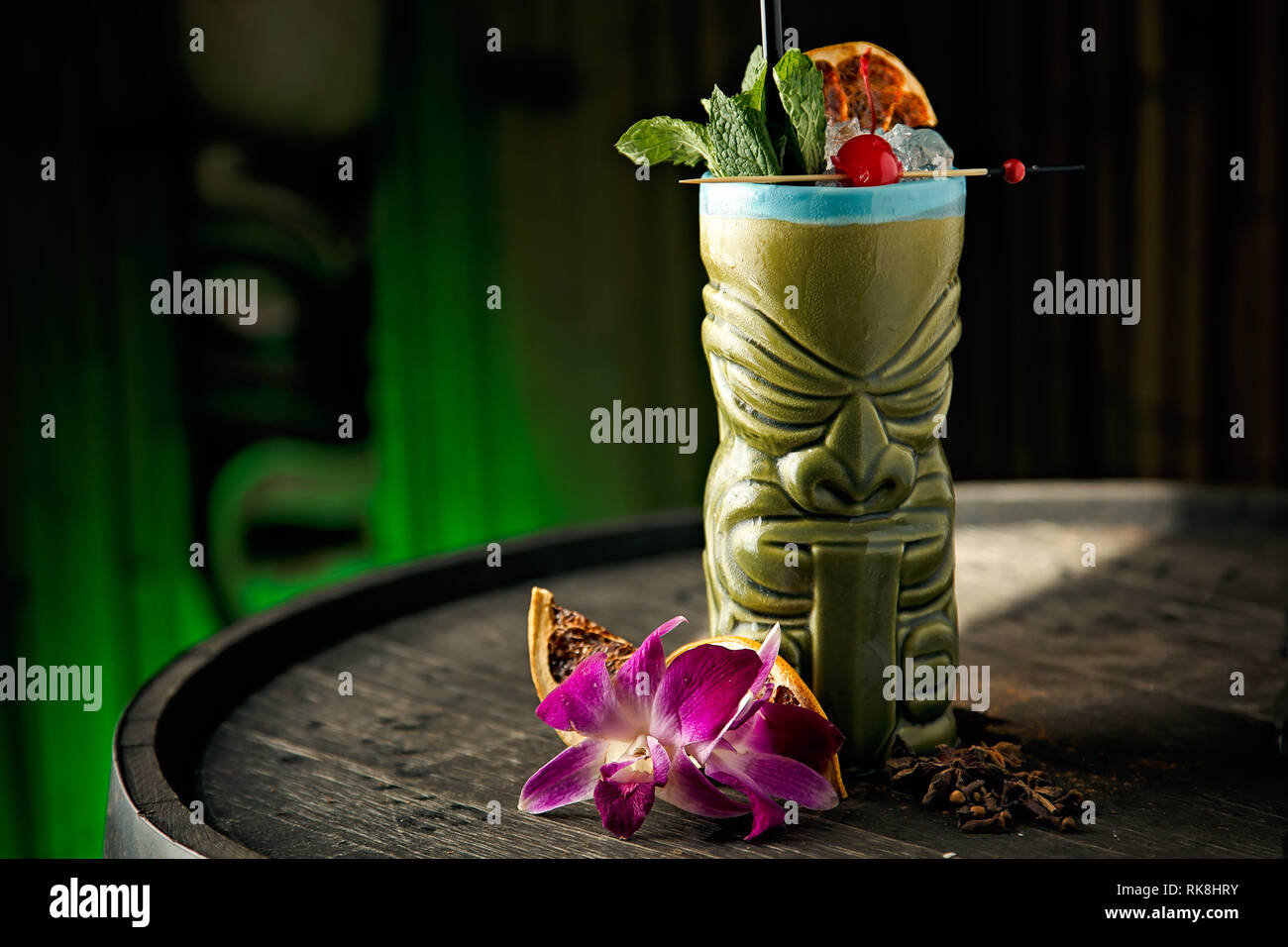 Fruity and refreshing Tiki drink served in a green Tiki Mug with a mint, cherry, and dry orange as garnishes Stock Photo