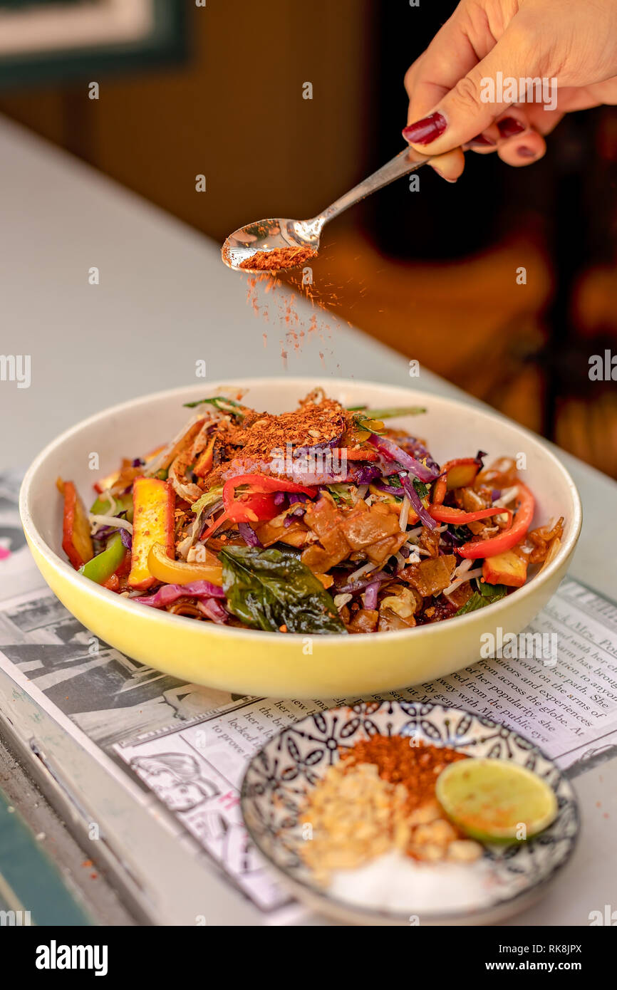 A lady's hand sprinkling spices from the spoon over a Thai dish Stock Photo