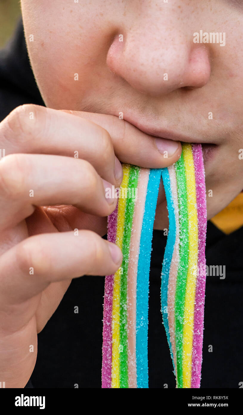 Child eat jelly colorful candy with sugar. Close-up child face and candy. Rainbow colours. Stock Photo